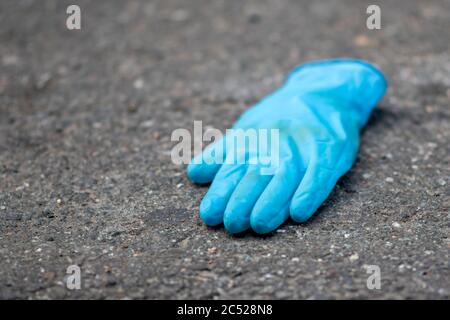 Blue medical glove isolated on dirty ground. Public health hazard amid coronavirus pandemic. Stock Photo