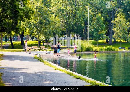 Montreal, Canada - June, 2018: Canadian family having fun in the pond and playing with their dog in La Fontaine park in Montreal, Quebec, Canada. Stock Photo