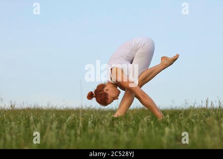 Yoga balance in nature. Concentrated young woman practicing morning yoga on meadow. Beautiful girl doing forward bend exercise outdoors Stock Photo