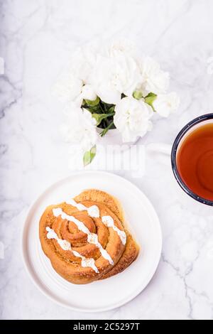 Homemade cinnamon bun on white plate and black tea on the white marble background. Flat lay Stock Photo