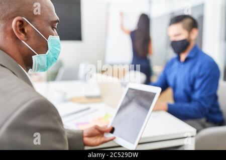 African business man using tablet computer and mask in office together with colleague Stock Photo