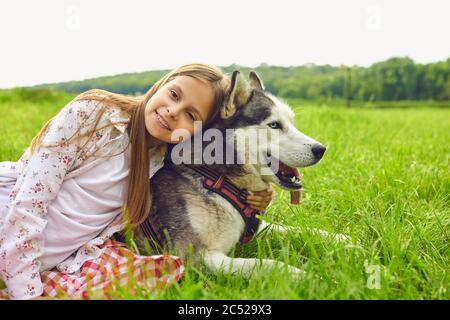 A little girl and a husky dog are hugging in a summer park on nature at the day time at the weekend. Stock Photo