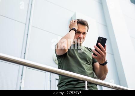 Confused man complaining after mistake checking mobile phone content in the street Stock Photo