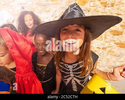 Portrait of a girl in the group of Halloween costume dressed kids standing together with buckets of candies Stock Photo