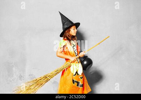 Portrait of a girl in Halloween costume stand with broom and bucket over the wall Stock Photo