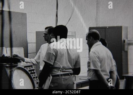 Fine 70s vintage black and white lifestyle photography of three men discussing a radar super computer assembly. Stock Photo