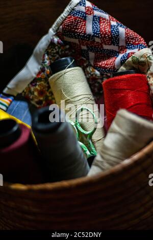 Vertical shot of colorful threads and small green scissors in the basket Stock Photo