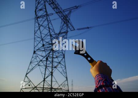 Industry and power line maintenance concept. Wrench in hand with silhouette of electric pylon in background. Energy network service. Stock Photo