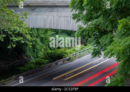 Long exposure photo of concrete bridge in a forested woods area with streaks of yellow and red light from fast cars on the highway. Stock Photo