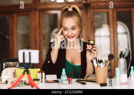 Pretty smiling girl holding rouge in hand showing how to make up while recording new video for her vlog Stock Photo