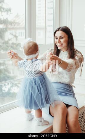 Smiling mother sitting  on a window sill playing with her baby daughter