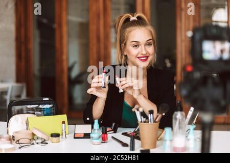 Nice smiling beauty blogger joyfully holding lipsticks in hands while recording new video for vlog Stock Photo