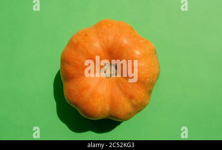 Fresh orange pumpkin isolated on green background. Top view. Raw mini pumpkin. Stock Photo