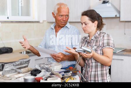 Confused woman with her elderly father reading work manual on mixer tap installation during overhaul at home Stock Photo