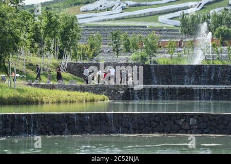 Ulanhot, China's Inner Mongolia Autonomous Region. 30th June, 2020. Tourists enjoy their leisure time on the bank of a man-made lake at Tianjun Mountain scenic spot in Ulanhot City, north China's Inner Mongolia Autonomous Region, June 30, 2020. Tianjun Mountain, located in the suburb of Ulanhot, was once cratered and lack of vegetation due to the extraction of stones in the past time. In recent years, the local government is committed to ecological restoration and has transformed the barren mountain into a scenic spot to boost local tourism. Credit: Liu Lei/Xinhua/Alamy Live News Stock Photo