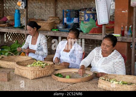 Ubud, Bali / Indonesia: Group of Indonesian women in white hand weaving baskets at a small artisanal shop near the Sacred Monkey Forest. Stock Photo