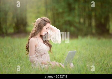 Woman sitting in a field working on her laptop, Thailand Stock Photo