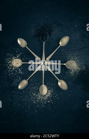 Antique silver spoons with various types of salts and spices laid out in patterns on a dark textured background Stock Photo