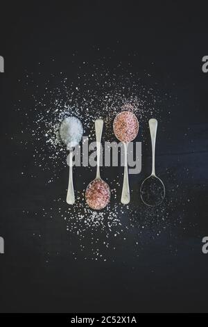 Antique silver spoons with various types of salts and spices laid out in patterns on a dark textured background Stock Photo
