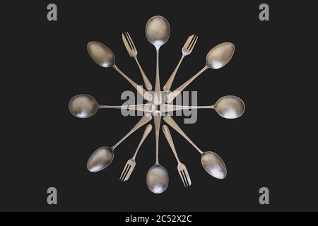 Antique silver spoons and forks laid out in patterns on a dark textured background Stock Photo