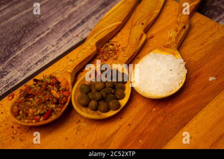 Large salt and various ground spices in wooden spoons on a wooden Board. Close up Stock Photo