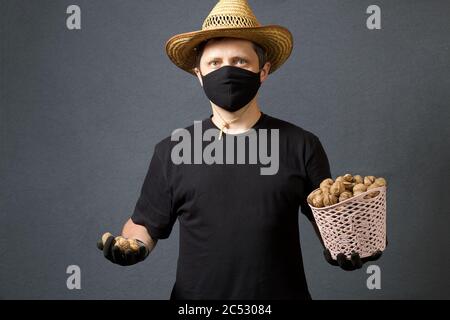 A farmer in a straw hat and a protective mask holds in his hand a wicker basket with walnuts. He holds a few nuts in his other hand. On a gray backgro Stock Photo