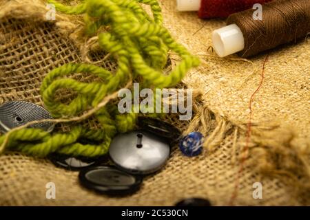 Various buttons and multicolored threads on coarse-textured burlap. Close up Stock Photo