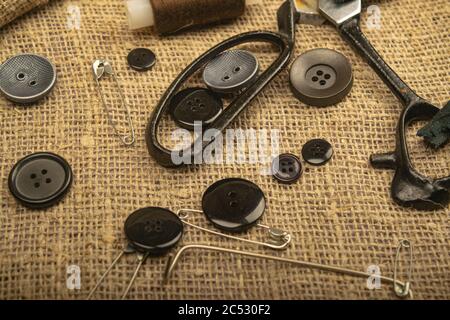 Pins of various sizes, tailor's scissors, and various buttons on coarse-textured burlap. Close up Stock Photo
