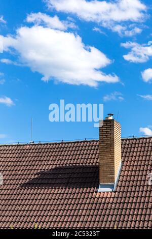 Brick chimney on the roof of a house against the blue sky. Environmental protection concept. Air pollution. Stock Photo