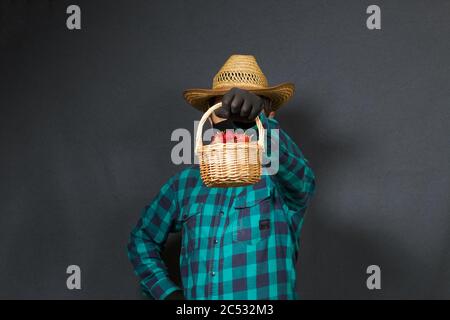 A man holds in front of him an outstretched basket of strawberries. Farmer with a protective mask on his face. There is a straw hat on his head. Shot Stock Photo