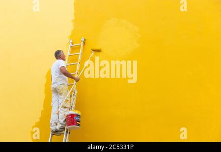 Man painting house wall yellow. Stock Photo