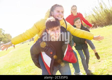 Happy teenage friends having fun together in spring city park, boys piggybacking girls Stock Photo