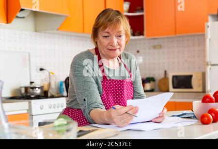Thoughtful middle aged woman sitting with paper documents in cozy home kitchen Stock Photo