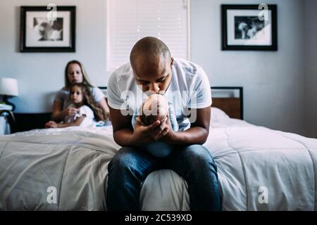 Center portrait of dad kissing newborn baby on bed Stock Photo