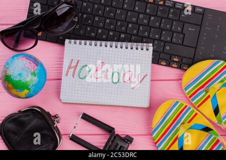 Holiday on notebook with woman's traveler accessories glasses wallet and flip-flops on pink table top background. Stock Photo