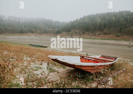 Anchored abandoned old fishing red boat on the bank of the empty Orlík Reservoir in foggy autumn day Stock Photo