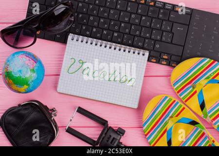 Vacation on notebook with woman's traveler accessories glasses wallet and flip-flops on pink table top background. Stock Photo