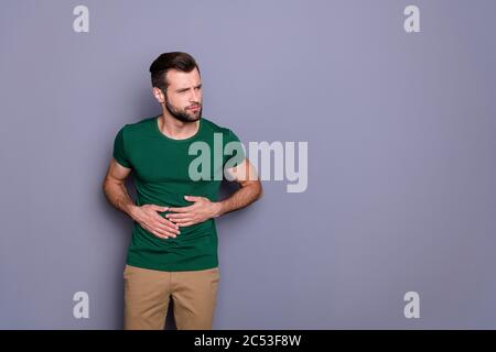 Portrait of frustrated man eat something wrong suffer stomach ache gastritis syndrome wear green pants trousers isolated over gray color background Stock Photo