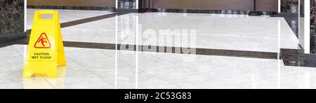 Marble shiny floor in a luxury hallway of company or hotel during cleaning. Panorama of a washed cleaned floor with sign of caution wet floor. Profess Stock Photo