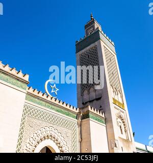 Low angle view of the 33-meter high minaret of the Great Mosque of Paris, France, with the star and crescent above the doorway against blue sky. Stock Photo