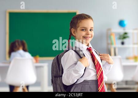 Back to school. Portrait of happy little girl with backpack and uniform standing in classroom, copy space Stock Photo