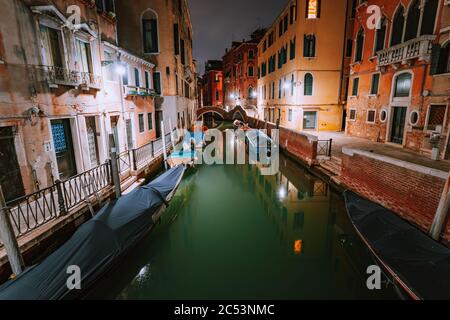 Venezia Italy. Narrow channel and gondola boats in lagoon city venice at night. Vivid colored old brick buildings around. Stock Photo