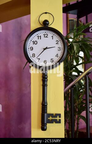 A clock shaped like an old antique key against a bright yellow tall pillar in the store Stock Photo