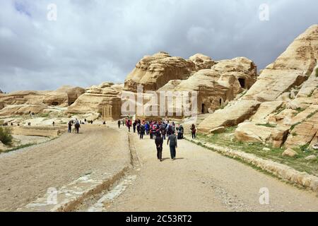 PETRA, JORDAN - APR 1, 2015: Tourists walking to Siq canyon in Petra. Petra's temples, tombs, theaters and other buildings are scattered over 400 squa Stock Photo