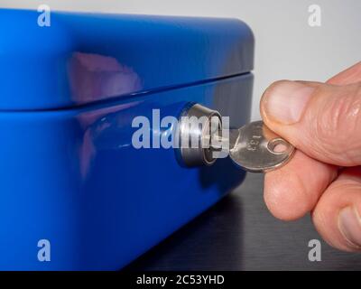A man’s fingers turning the numbered key in the lock of a blue painted metal, personal security box / safe. Stock Photo