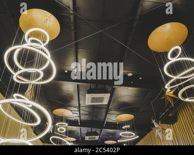 Bright LED lights in the shape of rings suspended on a black ceiling in the style of a loft Stock Photo