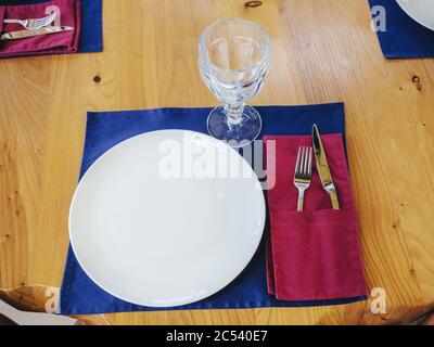 White plate with a crystal glass fork and knife on a blue napkin on a wooden light table. New shiny cutlery. Closeup photo Stock Photo