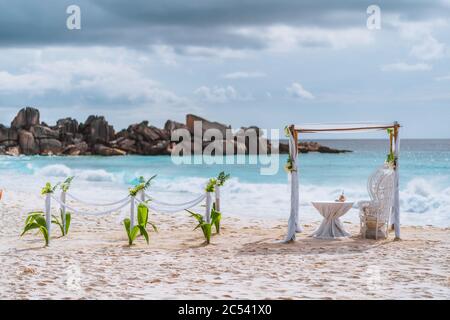 Decorated romantic wedding setting with table and chairs on sandy tropical beach in sunset light with moody clouds in background, Seychelles islands. Stock Photo