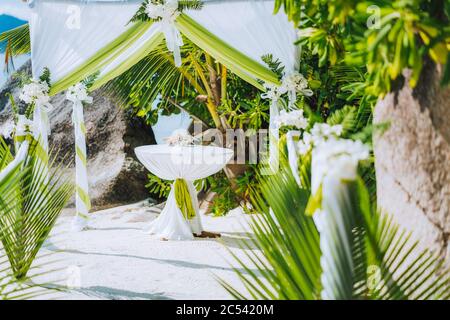 Decorated romantic wedding celebration location, table and chairs on tropical beach. Lush green foliage and white lowers. Stock Photo