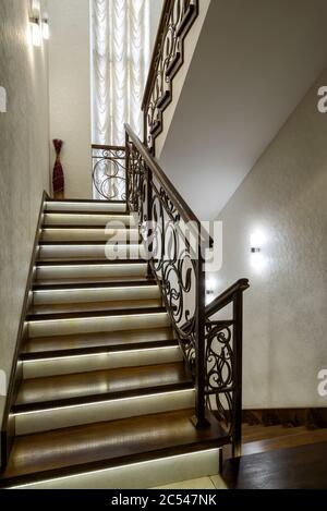 Interior of residential house or hotel. Nice staircase with LED lights. Home interior design in modern style. Contemporary wooden stairs with forged r Stock Photo